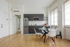Een moderne keuken met grijze kastjes, een magnetron en een koelkast. Er is een eettafel met stoelen en een glazen blad.