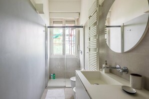 Een moderne badkamer met een douchecabine van glas, een wit wastafeltje en een grote spiegel.