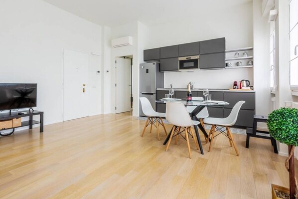 Een moderne keuken met donkere kastjes, een ingebouwde magnetron en een eethoek met een tafel en stoelen.
