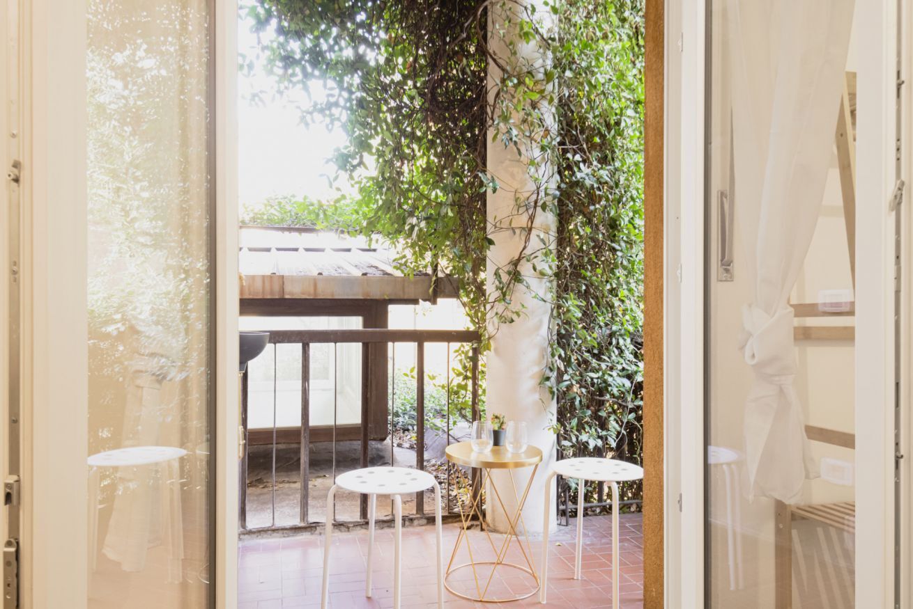 An open doorway leading to an outdoor patio with a wooden pergola, two round tables, and a bench.