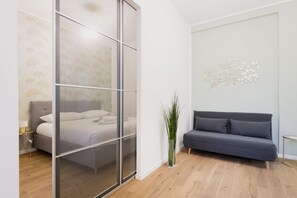 A modern bedroom with a bed, a grey sofa, a glass partition, and a wall art piece. - Easylife - Stylish abode a few steps from Navigli (Milano)