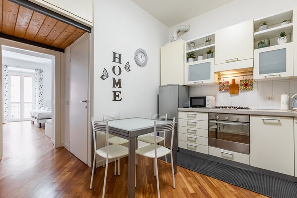 A compact kitchen with white cabinets, a microwave, an oven, and a dining area with a table and chairs.