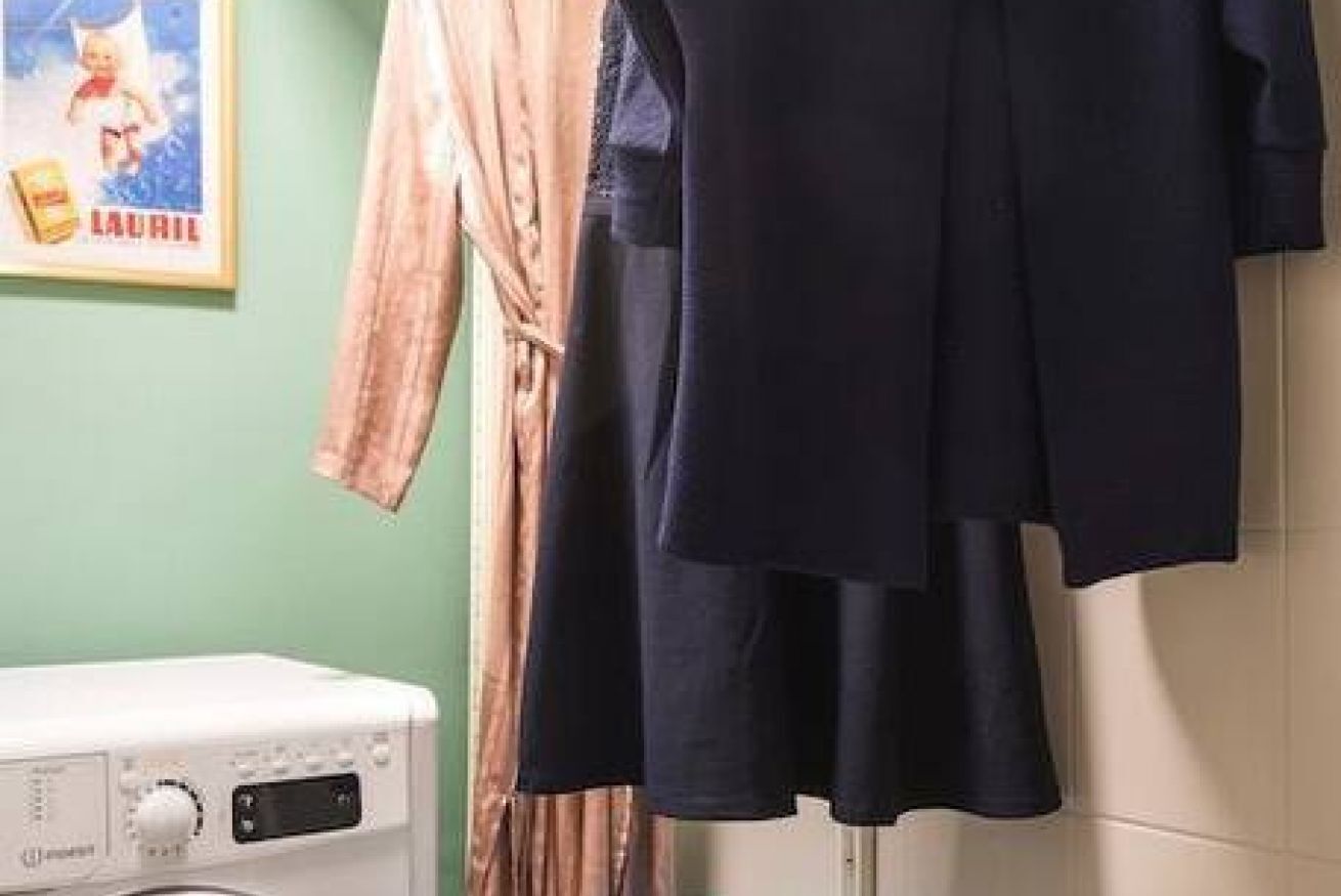 A laundry room with a washing machine, a drying rack, and a poster on the wall.