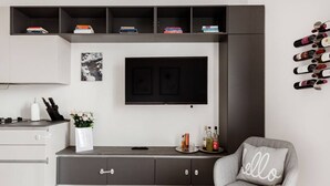 A modern living room with a flat-screen TV mounted on the wall, a grey armchair with a pillow, a console table with books and bottles, and a wine rack on the wall. - Easylife - Apartment with a refined style (Milano)