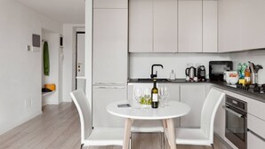 A modern kitchen with white cabinets, a round dining table with two chairs, a wine bottle, and glasses. - Easylife - Apartment with a refined style (Milano)