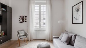 A modern living room with a grey sofa, a round ottoman, a grey chair with a 'hello' pillow, a black cabinet, and a window with white curtains. - Easylife - Apartment with a refined style (Milano)