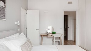 A bedroom with a bed, a desk with a chair, a mirror, and a door leading to another room. - Easylife - Apartment with a refined style (Milano)