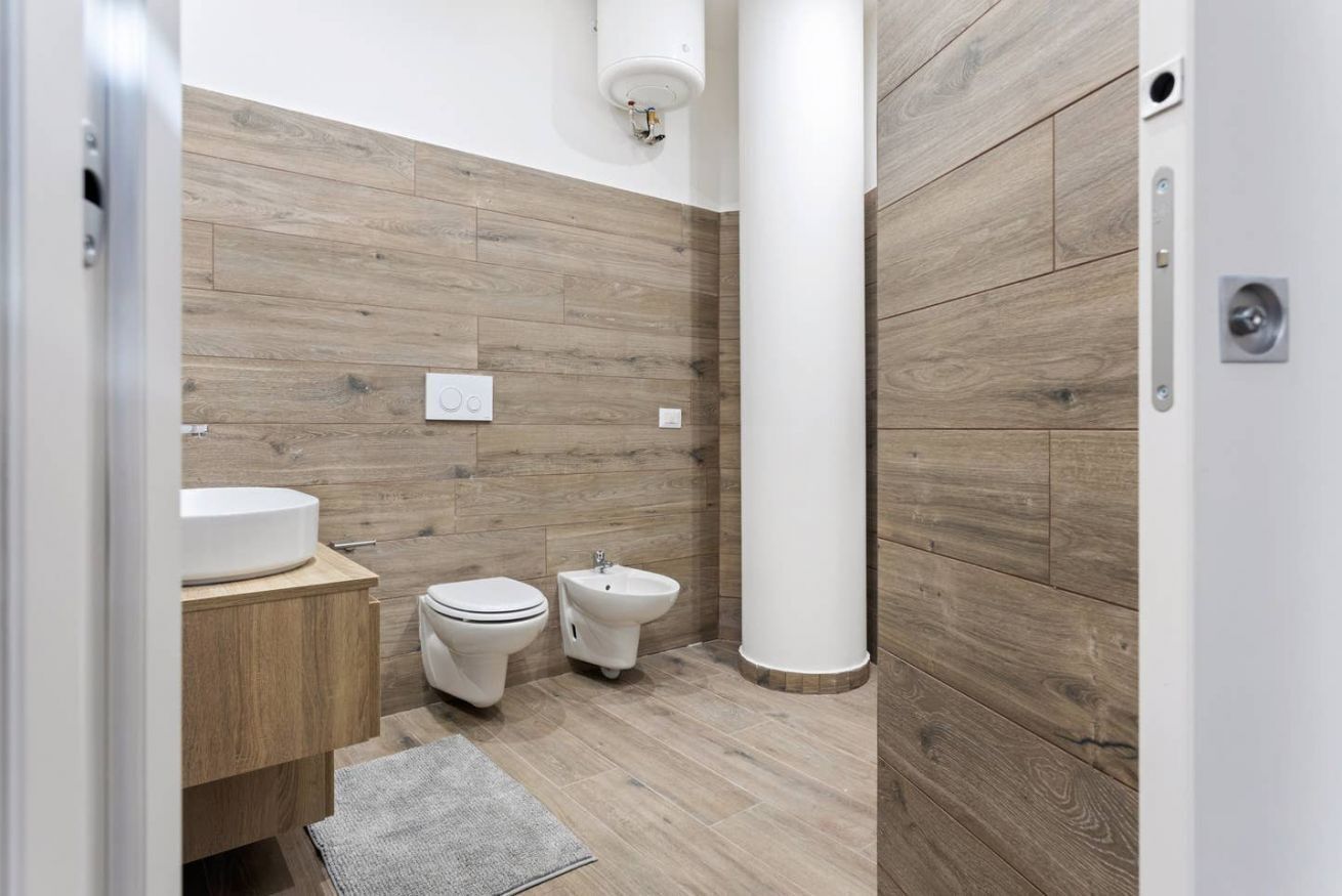 A modern bathroom with a wooden wall panel, a toilet, a bidet, and a sink.