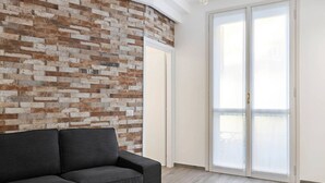 A modern living room with a grey sofa, a brick-patterned wall, and a sliding glass door leading to a balcony. - Easylife - Modern and new flat in Duomo area (Milano)