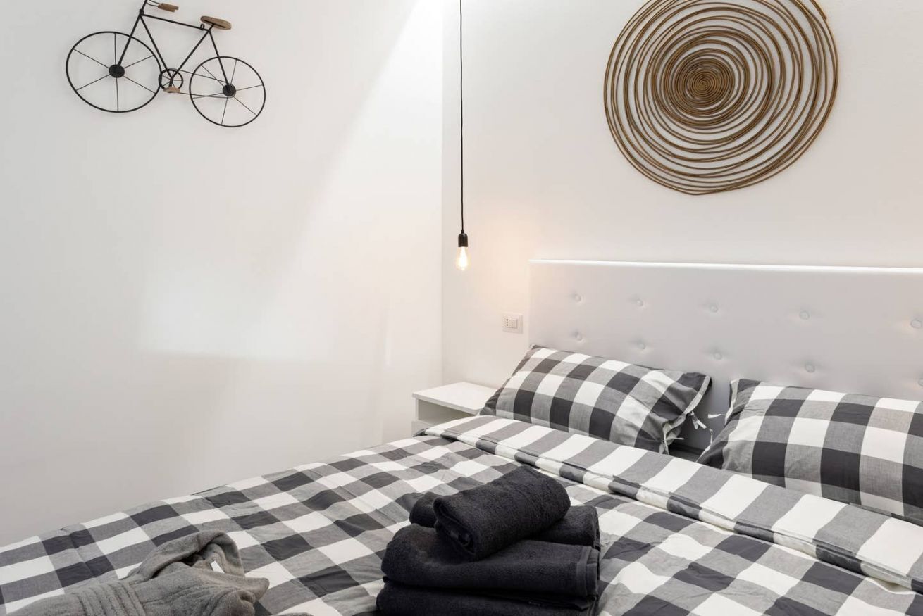 Une chambre moderne avec une couvre-lit à carreaux, une décoration murale représentant un vélo, un élément décoratif circulaire au mur et une lampe de chevet.