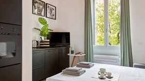A modern hotel room with a bed, a TV, a small table with a plant, and a window with curtains.