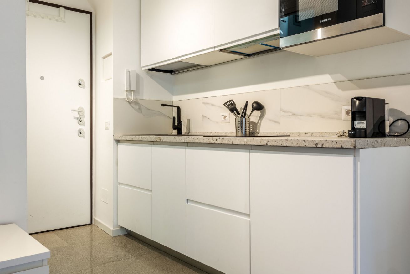 A modern kitchen with white cabinets, a marble countertop, and a built-in microwave.