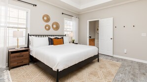 Un dormitorio con cama, mesitas de noche, una alfombra y una puerta que da a otra habitación.