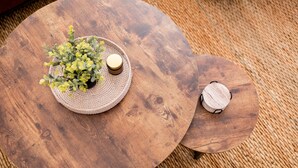 Dos mesas de madera con individuales tejidos, una con una pequeña planta y una vela, y la otra con una vela.