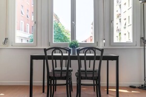 A dining area with a table and two chairs, a small plant on the table, and a window with a view of buildings and trees. - Easylife - Stylish and fancy flat in Buenos Aires (Milano)