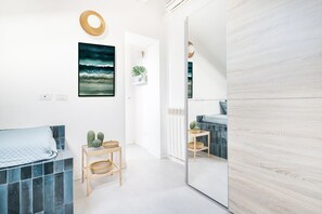 A modern bedroom with a bed, a mirror, a wall art, a small table with plants, and a door leading to another room. - Easylife - Nice studio apartment in Buenos Aires area (Milano)