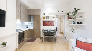 A modern kitchen with a dining area, a white wall with shelves, and a small plant on the floor.
