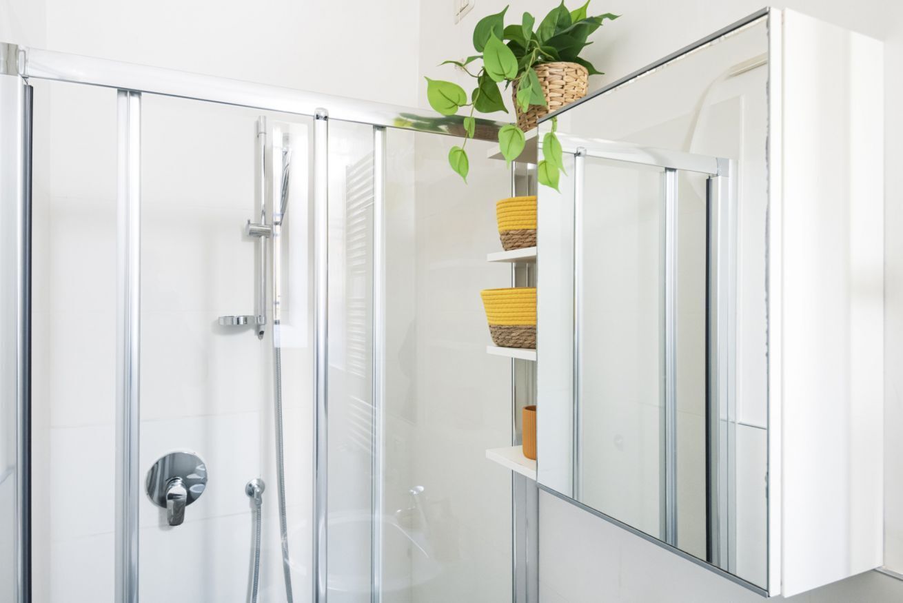 Een moderne badkamer met een douchecabine van glas, een spiegel en planken met gevlochten manden.