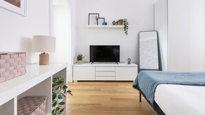 Ett modernt sovrum med en säng, en tv, en hylla med dekorativa föremål och en växt.