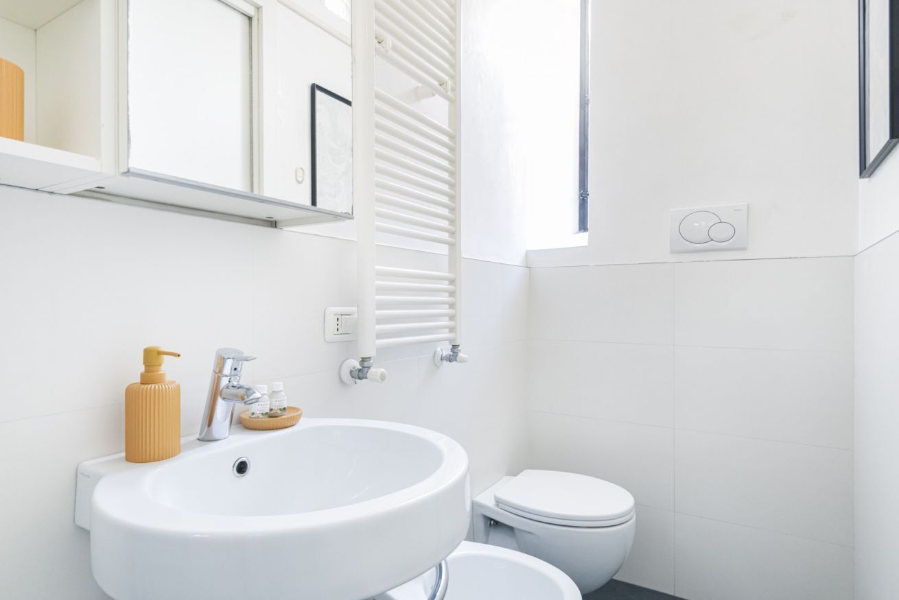 A modern bathroom with a white sink, a toilet, and a window.