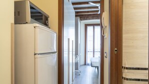 A narrow hallway with a refrigerator on the left, a wooden door on the right, and a window at the end. - Easylife - Intimate retreat in Porta Venezia (Milano)