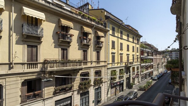 A row of multi-story buildings with balconies, a street in the foreground, and parked cars. - Easylife - Intimate retreat in Porta Venezia (Milano)