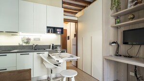 A modern kitchen with white cabinetry, a dining area with a white table and stools, and a TV mounted on a wooden shelf. - Easylife - Intimate retreat in Porta Venezia (Milano)