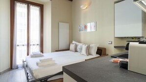 A bedroom with a bed, a bedside table, a window with curtains, a wall-mounted light, and a small shelf. - Easylife - Intimate retreat in Porta Venezia (Milano)