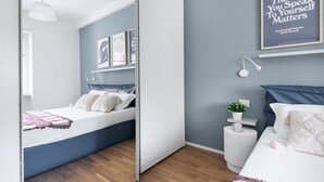 Une chambre à coucher moderne avec un lit, des tables de chevet, une étagère murale ornée de tableaux encadrés, une lampe de chevet et une citation inspirante sur le mur.