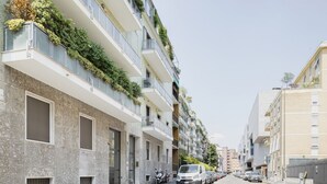 Un immeuble résidentiel à plusieurs étages, doté de balcons, donnant sur la rue et avec des voitures garées devant.
