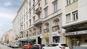 Une rangée d’immeubles à plusieurs étages, dont le rez-de-chaussée abrite divers commerces, notamment une boutique de glaces et un magasin de tabac.