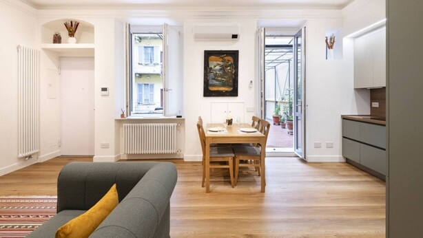 Un salon moderne avec un canapé gris, une table à manger en bois et un coin cuisine doté de meubles gris.