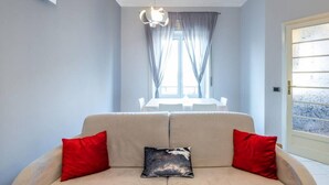 A living room with a beige sofa, red cushions, a modern pendant light, a window with curtains, and a view of a snowy landscape.