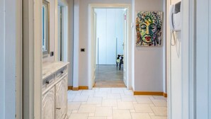 A hallway with a white tiled floor, a white door at the end, and a painting on the wall.