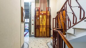 A hallway with a metal elevator, a wooden staircase, and a tiled floor.