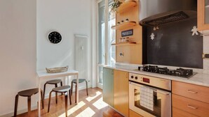 A modern kitchen with a gas stove, oven, and wooden cabinets. There is a small dining area with two stools and a table. - Easylife -Amazing flat Repubblica Central Station (Milano)