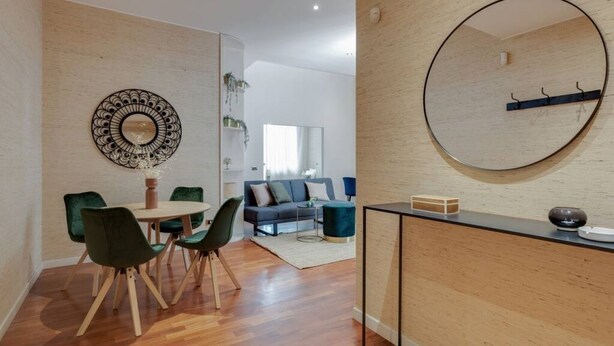 A modern living room with a wooden floor, a round mirror, a dining area with a table and chairs, and a blue sofa. - Easylife -Amazing flat Repubblica Central Station (Milano)