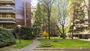 A courtyard with a stone pathway, surrounded by greenery and trees. - Easylife - Style and comfort in Porta Venezia (Milano)