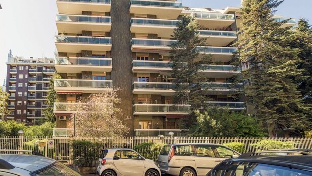A multi-story residential building with balconies, a central vertical feature, and parked cars in the foreground. - Easylife - Style and comfort in Porta Venezia (Milano)