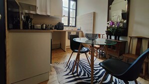 A compact kitchen with white cabinets, a coffee machine, and a window. There is a round glass table with a black chair and a zebra-patterned rug. - Historic Heart of Cahors!Elegant yet Cozy large 2 large bedroom apartment! (CAHORS)