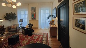 A living room with a chandelier, a sofa, a coffee table, and a rug. There are framed pictures on the wall and a plant in the corner. - Historic Heart of Cahors!Elegant yet Cozy large 2 large bedroom apartment! (CAHORS)