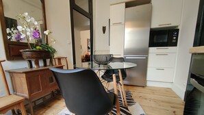 A modern kitchen with a refrigerator, microwave, and wooden cabinets. There is a dining table with chairs and a potted plant. - Historic Heart of Cahors!Elegant yet Cozy large 2 large bedroom apartment! (CAHORS)