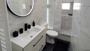 A modern bathroom with a white vanity, a round mirror, a toilet, and a shower area. - Historic Heart of Cahors!Elegant yet Cozy large 2 large bedroom apartment! (CAHORS)