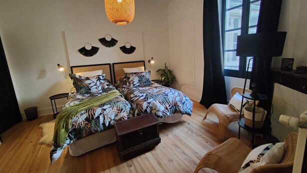 A bedroom with a bed, bedside tables, a chair, a hanging light fixture, and a window. - Historic Heart of Cahors!Elegant yet Cozy large 2 large bedroom apartment! (CAHORS)