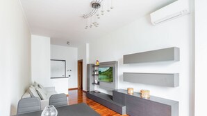 Una sala de estar moderna con piso de madera, sofás grises, una mesa de comedor y un televisor montado en la pared.