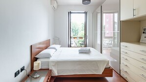 Un dormitorio con cama, lámpara de noche, armario y vistas al balcón exterior.