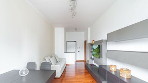 Una sala de estar moderna con una mesa de comedor, un sofá gris y un televisor de pantalla plana montado en la pared.