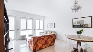 A spacious living area with a sofa, a dining table with chairs, and a chandelier.