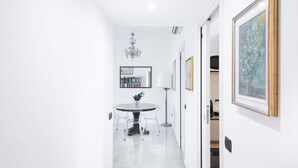A narrow hallway with a dining area featuring a round table and chairs, a chandelier, and framed artwork on the walls.