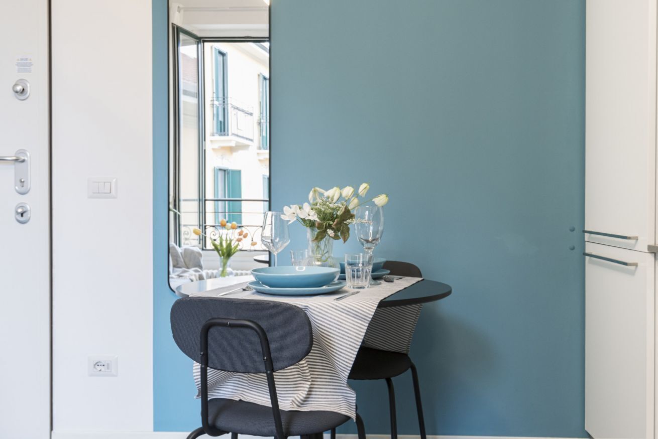 Comedor con una mesa lista para dos, con mantel a rayas, platos azules y un florero con flores blancas.
